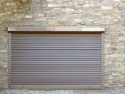 A window with brown metal rolling shutters. Wall decoration with artificial flatten stone