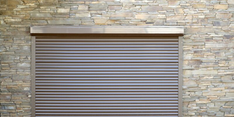 A window with brown metal rolling shutters. Wall decoration with artificial flatten stone