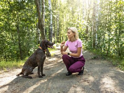 A young woman trains a dog in the forest