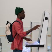 Concentrated African American man student stands near terminal to check class timetable in college