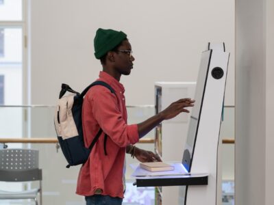 Concentrated African American man student stands near terminal to check class timetable in college
