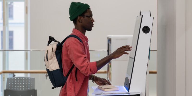 Concentrated African American man student stands near terminal to check class timetable in college