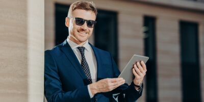 Happy male entrepreneur sends text message to colleague via touch pad