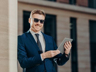 Happy male entrepreneur sends text message to colleague via touch pad