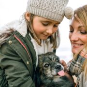 Mother and daughter stroking their dog on the beach in winter