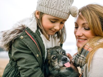 Mother and daughter stroking their dog on the beach in winter