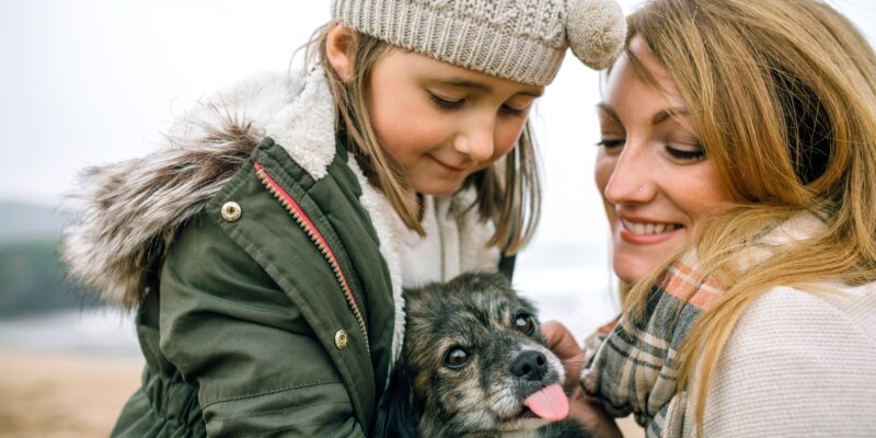 Mother and daughter stroking their dog on the beach in winter