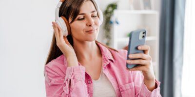 Smiling, beautiful woman listening music in earphones, using mobile phone, text message