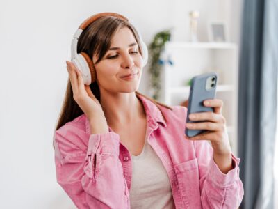 Smiling, beautiful woman listening music in earphones, using mobile phone, text message