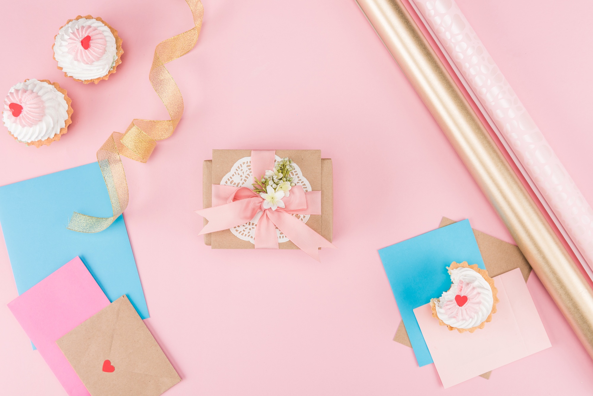 Top view of tasty cupcakes, blank cards, decorative envelope and wrapping paper on pink, birthday